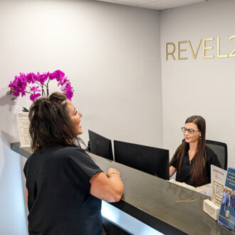 Two team members of Revel22 Wellness share a light-hearted moment at the front reception desk.